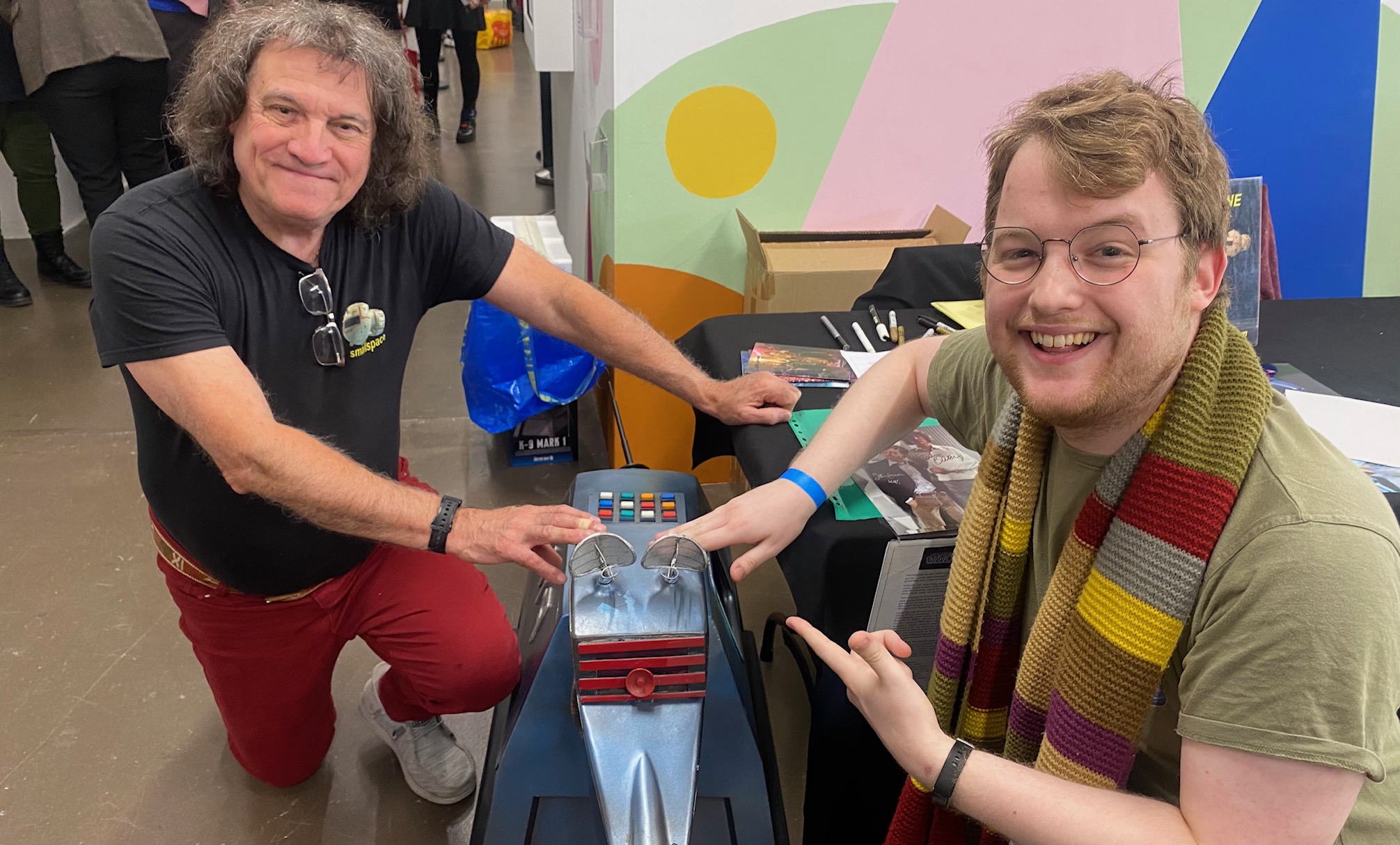 Harry, wearing a long multicoloured scarf, posing for a photo with K9, a robot dog, and Mat Irvine, a man with curly hair.