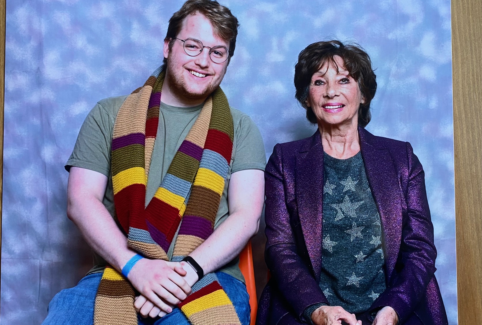 Harry and Carole Ann Ford, sitting in front of a blue backdrop and posing for a photo